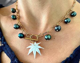 May include: A gold chain necklace with a white maple leaf pendant and dark green pearl accents.