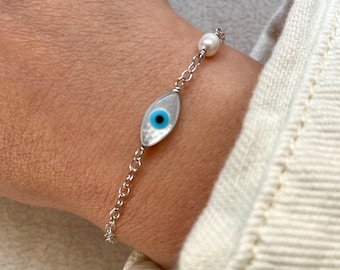 May include: A silver chain bracelet with a white pearl and a blue evil eye charm. The charm is made of white mother of pearl with a blue eye in the center.