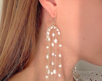May include: Elegant gold-tone earrings featuring a cascade of white pearls. The earrings have a curved top design with multiple strands of pearls and small, sparkling accents. The design is delicate and sophisticated, suitable for special occasions.