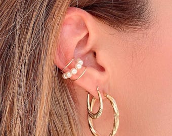 May include: Gold hoop earrings with a twisted design. The earrings are worn with a gold ear cuff with pearl accents.