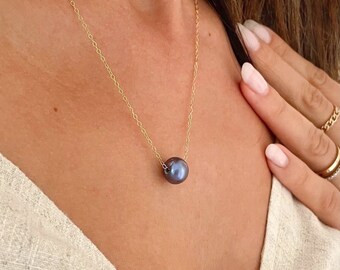 May include: A delicate gold chain necklace with a single, large, dark gray pearl pendant.