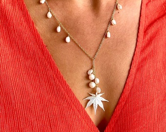 May include: A gold chain necklace with a white pearl pendant in the shape of a maple leaf. The necklace has multiple pearl drops along the chain.