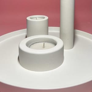 May include: A white ceramic tray with three white ceramic candle holders. The tray is round and has a raised edge. The candle holders are different sizes and have a smooth, matte finish.