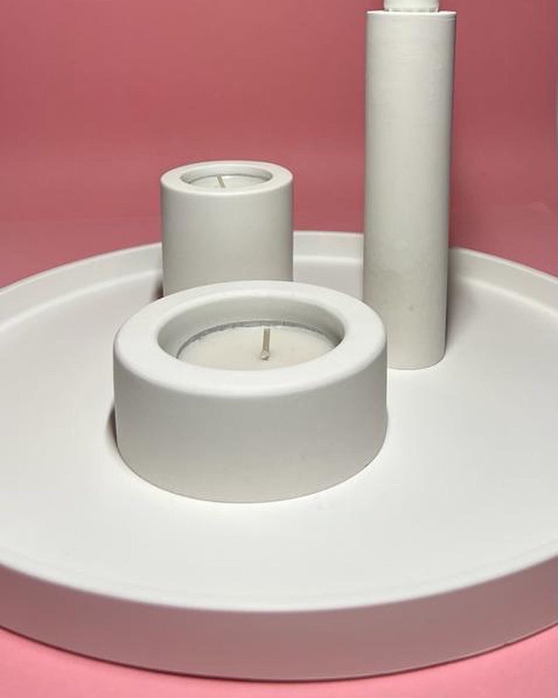 May include: A white ceramic tray with three white ceramic candle holders. The tray is round and has a raised edge. The candle holders are different sizes and have a smooth, matte finish.