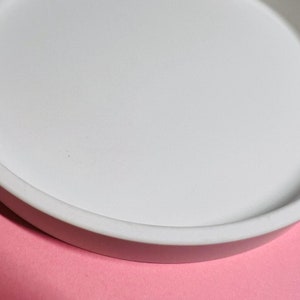 May include: A white ceramic tray with a rounded edge. The tray is on a pink surface.