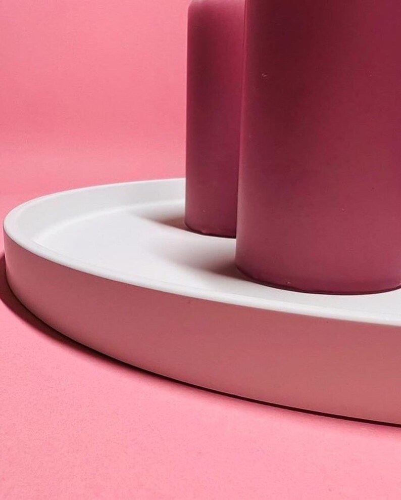 May include: Two tall pink candles on a white oval tray. The tray is on a pink background.
