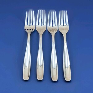 May include: Four silver forks arranged vertically against a solid blue background. The forks have a classic design with tines and elongated, teardrop-shaped handles. The polished metal reflects light, creating highlights.