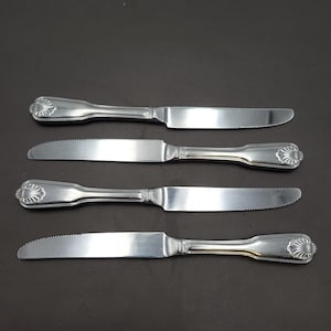 May include: Four stainless steel butter knives arranged horizontally. Two knives have a smooth blade, and two have a serrated blade. Each knife features a decorative handle with a shell-like design at the end.