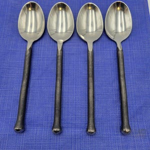 May include: Four stainless steel spoons with dark gray textured handles are arranged on a blue surface. The spoons have a classic oval bowl shape and a sleek, modern design. The handles have a slightly rough texture.
