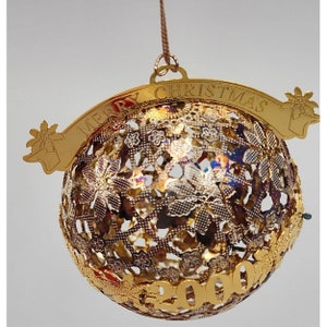 Könnte beinhalten: Goldfarbener Weihnachtsbaumschmuck mit einem filigranen, komplizierten Design. Der Schmuck besteht aus einer runden, durchbrochenen Kugel mit einem Banner, auf dem "Merry Christmas" steht. Das Jahr "2000" ist auf die Kugel eingraviert.