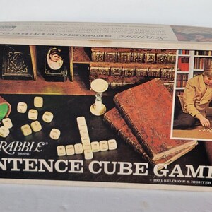 May include: A vintage Scrabble Sentence Cube Game box with a brown and white design. The box features the Scrabble logo and the text "Sentence Cube Game". The box is open and shows the game pieces, a timer, and a book.