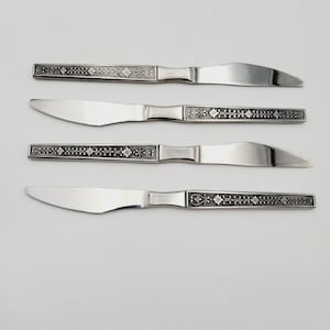 May include: Four silver dinner knives with black floral designs on the handles.