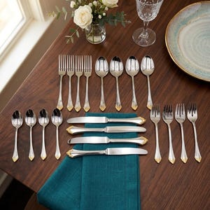 May include: A stainless steel flatware set featuring four dinner forks, four dinner spoons, four salad forks, four teaspoons, and four dinner knives. Each piece has a polished silver finish with a gold-toned accent at the base of the handle.