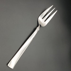 Può includere: Una forchetta d'argento con un design semplice. La forchetta ha tre denti e un manico lungo e sottile.