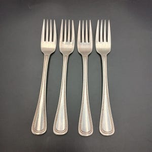 May include: Four silver forks with beaded handles. The forks are arranged in a row, with the tines facing up.