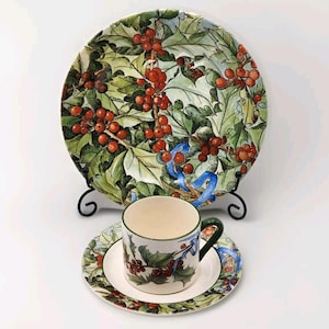 May include: A set of three ceramic plates featuring a holly and berry design. The plates are white with green leaves and red berries. The largest plate is a dinner plate, the middle plate is a salad plate, and the smallest plate is a saucer.