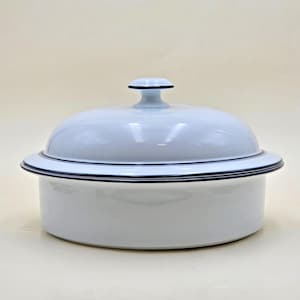 May include: A round, white enamel casserole dish with a matching domed lid. The piece features a smooth, glossy finish and is accented with a thin, dark navy blue rim along the edge of the lid, the base of the lid, and the top edge of the pot.