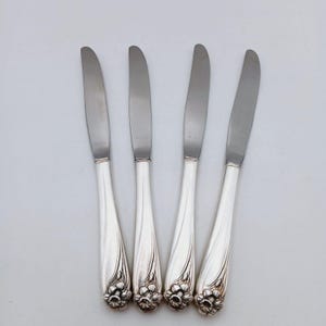 Könnte beinhalten: Vier silberne Essmesser mit Blumendesigns auf den Griffen.