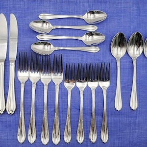 May include: A set of polished silverware, including knives, forks, and spoons, arranged on a blue surface. The set includes various sizes of spoons and forks, with a matching design on the handles. The silverware is likely for dining.