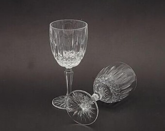 May include: Two clear glass wine glasses with a cut crystal design. The glasses are empty and sitting on a black surface.