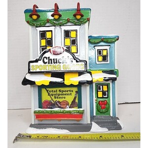 Pu&ograve; includere: Un edificio in miniatura con un tetto verde e un cartello che recita "Chuck's Sporting Goods". L'edificio ha una vetrina con un cartello che recita "Total Sports Equipment Store".