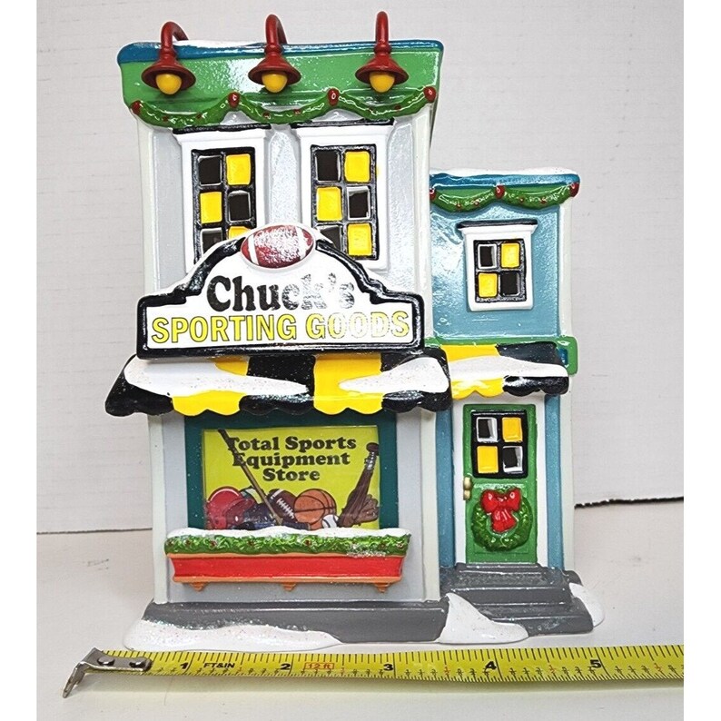Pu&ograve; includere: Un edificio in miniatura con un tetto verde e un cartello che recita "Chuck's Sporting Goods". L'edificio ha una vetrina con un cartello che recita "Total Sports Equipment Store".