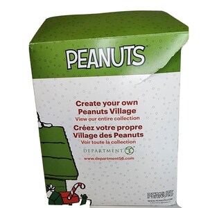 Pu&ograve; includere: Una scatola verde con sfondo bianco che presenta i personaggi dei Peanuts. La scatola ha il testo "Create your own Peanuts Village" e "View our entire collection". La scatola ha anche il testo "Cr&eacute;ez votre propre Village des Peanuts" e "Voir toute la collection". La scatola ha il testo "DEPARTMENT 56" e "www.department56.com". La scatola ha anche il testo "PEANUTS" e "www.PEANUTS.COM".