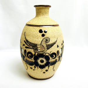 May include: A tan ceramic vase with a brown rim and a black and white bird design. The bird is surrounded by black and white floral designs.