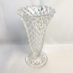 May include: Clear glass vase with a diamond pattern and a flared, ruffled top. The vase has a round base and a conical shape, suitable for displaying flowers or as a decorative piece.