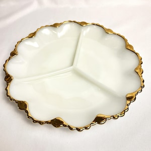May include: A white, three-sectioned serving dish with a scalloped edge and gold trim. The dish has a glossy finish and is designed for serving appetizers or snacks. The gold trim adds a touch of elegance to the piece.