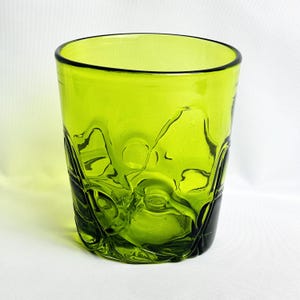 May include: A lime green glass tumbler featuring a thick, smooth rim and a textured, organic exterior surface with irregular, rounded indentations and raised glass formations that create a dynamic, rippled appearance throughout the body.