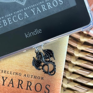 May include: A black Kindle e-reader with a black dragon bookmark. The Kindle screen displays the text "New York Times Bestselling Author Rebecca Yarros".