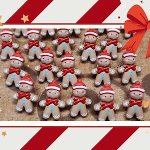 May include: A collection of small, tan gingerbread man figurines, each wearing a red and white hat and a red scarf. The figures have painted blue buttons on their chests and smiling faces. They are arranged in a grid pattern on a textured surface.