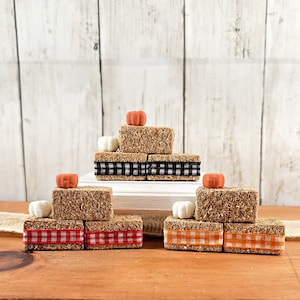 May include: Three miniature hay bale stacks decorated with orange and white pumpkins and black and white, red and white, and orange and white checkered ribbon.