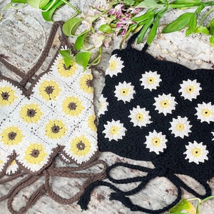 May include: Two crocheted tops with daisy flower designs. One top is white with brown accents and the other is black with white accents.