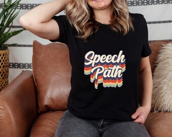 Può includere: Una maglietta nera con una grafica in stile retrò che dice "Speech Path" in lettere colorate e sovrapposte.