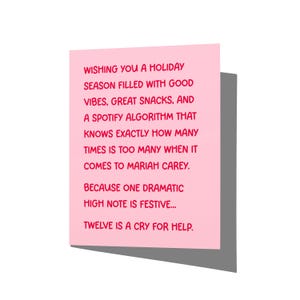 May include: A light pink greeting card with red text that reads: WISHING YOU A HOLIDAY SEASON FILLED WITH GOOD VIBES, GREAT SNACKS, AND A SPOTIFY ALGORITHM THAT KNOWS EXACTLY HOW MANY TIMES IS TOO MANY WHEN IT COMES TO MARIAH CAREY. BECAUSE ONE DRAMATIC HIGH NOTE IS FESTIVE... TWELVE IS A CRY FOR HELP.