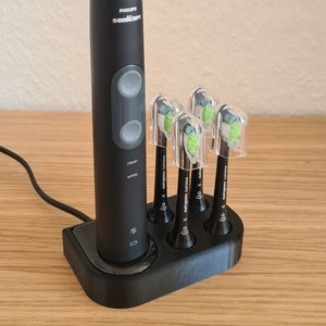 Könnte beinhalten: Eine schwarze elektrische Zahnbürste mit einer Ladestation und fünf Ersatzbürstenköpfen. Die Zahnbürste hat einen weißen Knopf und den Text "clean white" auf der Vorderseite. Die Bürstenköpfe sind mit "Philips Sonicare" beschriftet.