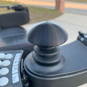 Peut inclure: Gros plan sur un joystick de commande noir avec un dessus en forme de dôme texturé. Le joystick est monté sur une base noire avec une série de boutons.