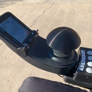 May include: A black joystick control with a round, black knob and a digital display screen. The control has several buttons, including a red button labeled "STOP".