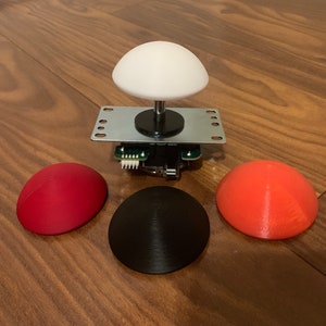 May include: Three arcade buttons, one black, one red and one orange, with a white joystick on top of a silver base.