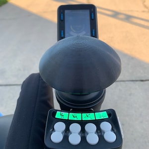 May include: A black control panel with five buttons and four green lit icons depicting a person sitting in a chair. The control panel is attached to a black, round, textured base.