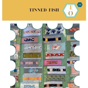 May include: A quilt pattern called "Tinned Fish" by Textile Outpost. The quilt is made of colourful fabric scraps in a variety of patterns and colours, including green, red, yellow, blue, and white. The quilt is framed by a white border with a scalloped edge.