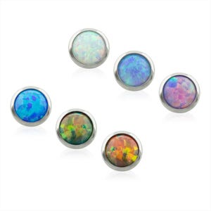May include: A collection of six circular stud earrings featuring polished silver-tone metal settings. Each stud contains a smooth, domed cabochon stone with a vibrant, iridescent finish in various colors including white, blue, pink, green, and orange.