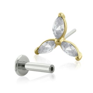 May include: A gold-toned body jewelry stud featuring three marquise-cut clear stones arranged in a floral cluster design. The piece includes a separate flat-back post with a silver-toned metallic finish, designed for secure insertion and comfortable wear.