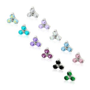 May include: A collection of eleven metal body jewelry studs, each featuring a triangular base set with three round faceted gemstones in various colors including clear, iridescent, blue, purple, pink, black, and green, arranged in a scattered pattern.