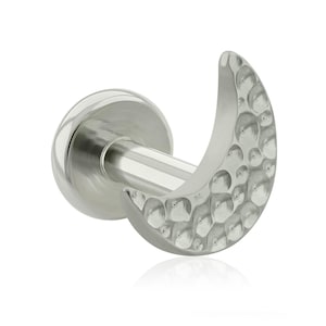 Puede incluir: Un pendiente plateado en forma de media luna con una superficie texturizada. El pendiente tiene un poste y una parte trasera plana. La forma de la luna está detallada con una textura martillada, lo que le da una apariencia única y artesanal.