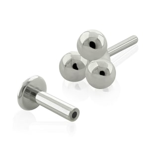 May include: A collection of silver-colored body jewelry. One piece features a flat disc with a straight post. The other piece has three small, shiny spheres attached to a straight post. The jewelry is displayed against a white background.