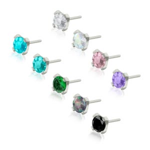 May include: A collection of nine stud earrings featuring round, faceted gemstones in various colours including clear, turquoise, light blue, pink, green, purple, iridescent, and black, each set in a four-prong silver-tone metal base with a post.