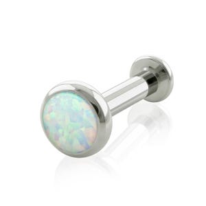May include: A silver-toned labret stud body jewelry piece featuring a circular flat back and a front setting containing a round, iridescent white opal cabochon with subtle flashes of blue, green, and pink light set in a polished metal bezel.